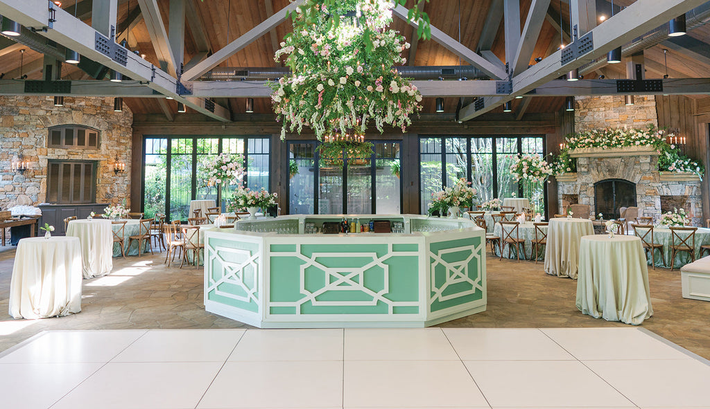 A green latticed bar under a large floral arrangement in a brick and wood room.