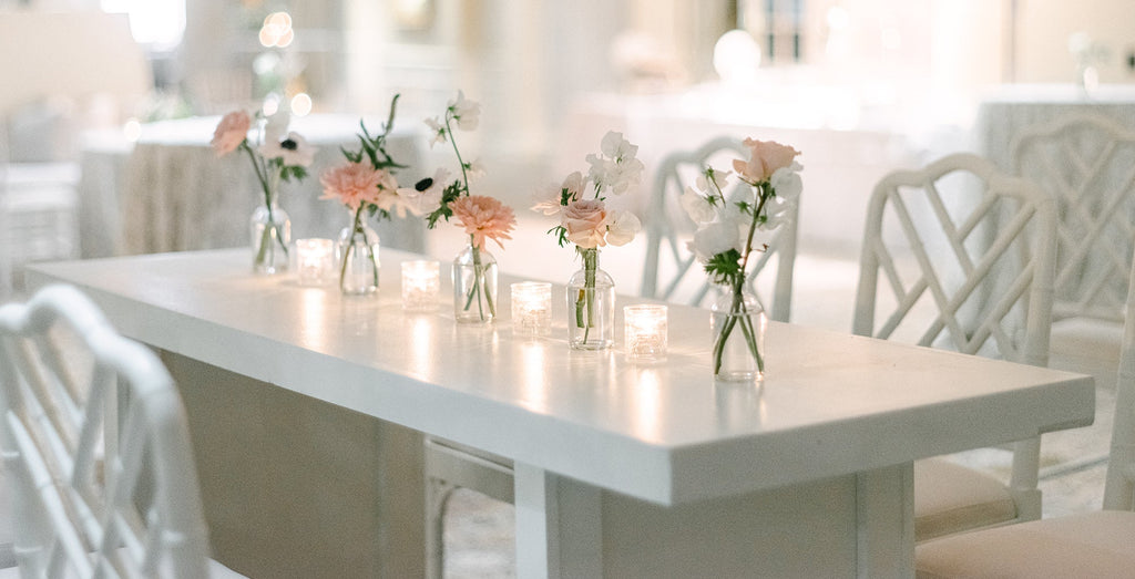A minimalist white table and chairs with pastel flowers and glass vases.