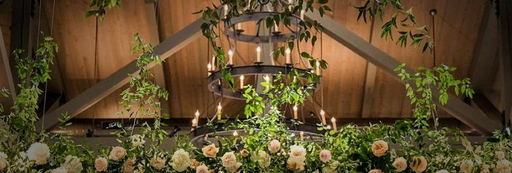 A wrought-iron chandelier and flowers under a wood ceiling.