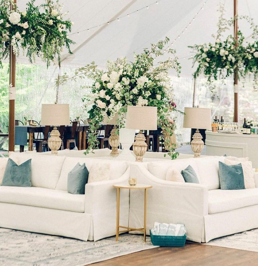 White sofas, lamps, and floral arrangements under a white tent.